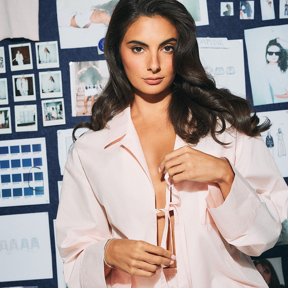 Woman in a light pink robe standing in front of a wall with various images and text.