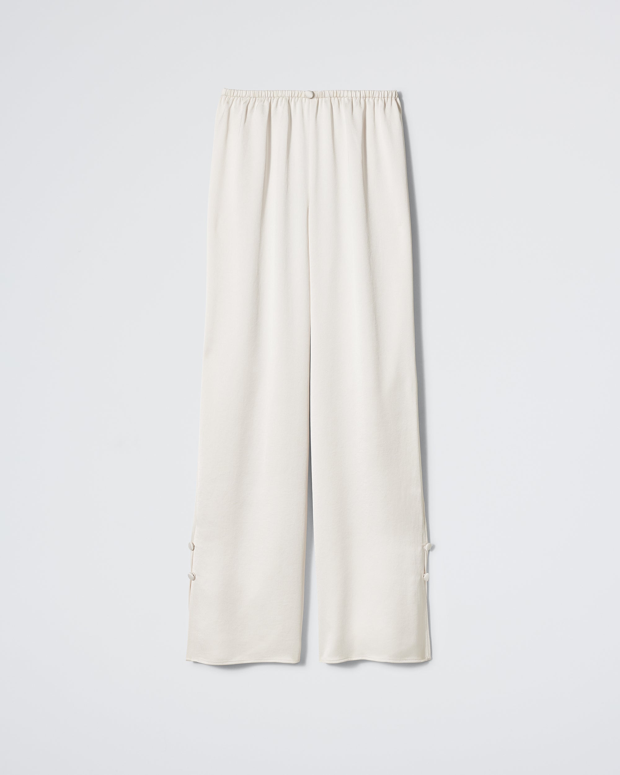 The Daphne After Party Pant in Champagne is a loose-fitting, high-waisted off-white pant featuring an elastic waistband and subtle decorative ties at the ankles, shown against a plain white background.