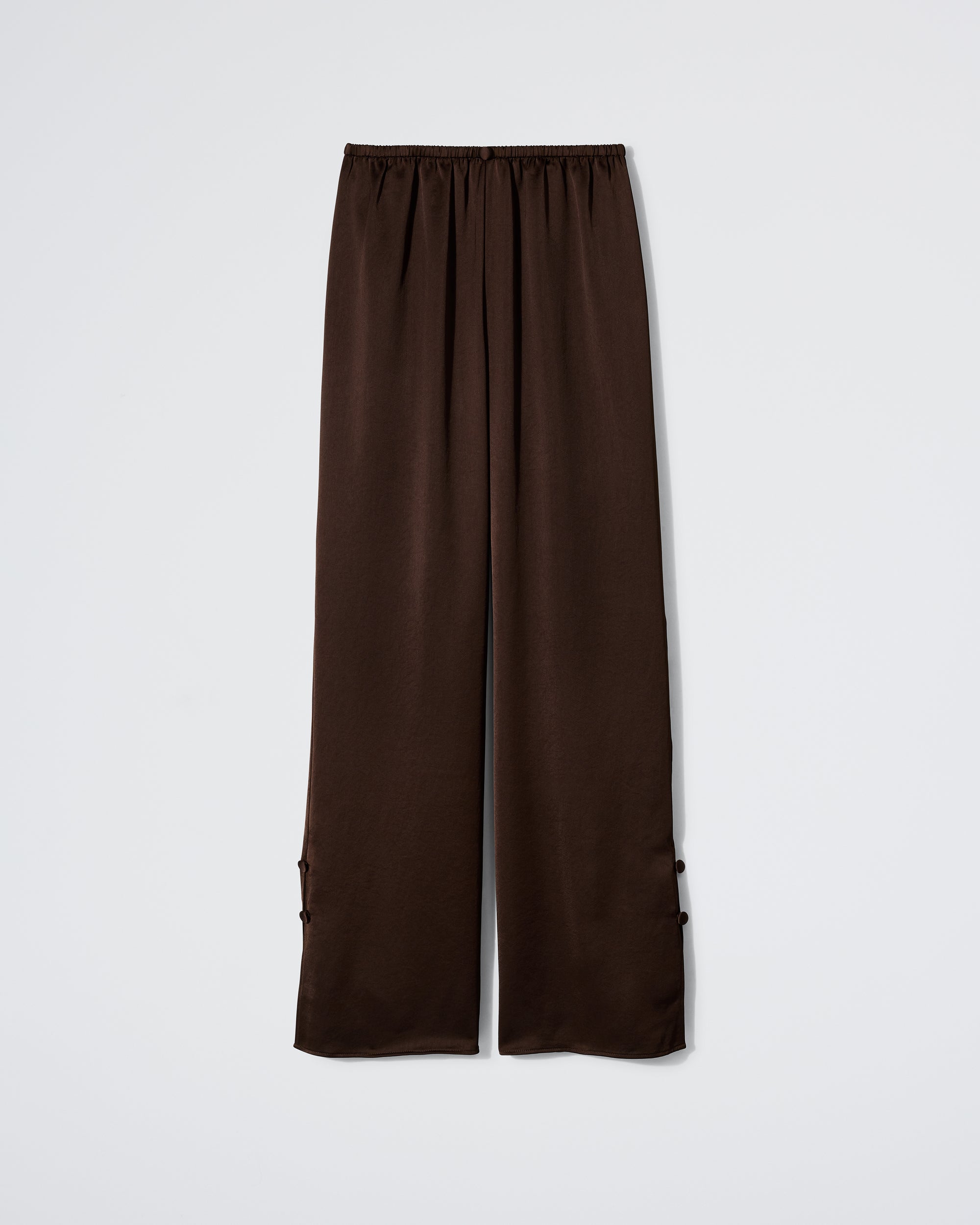 The Daphne "After Party Pant" in Espresso features a loose fit, satin fabric, elastic waistband, and button details near the ankles, shown against a plain white background.
