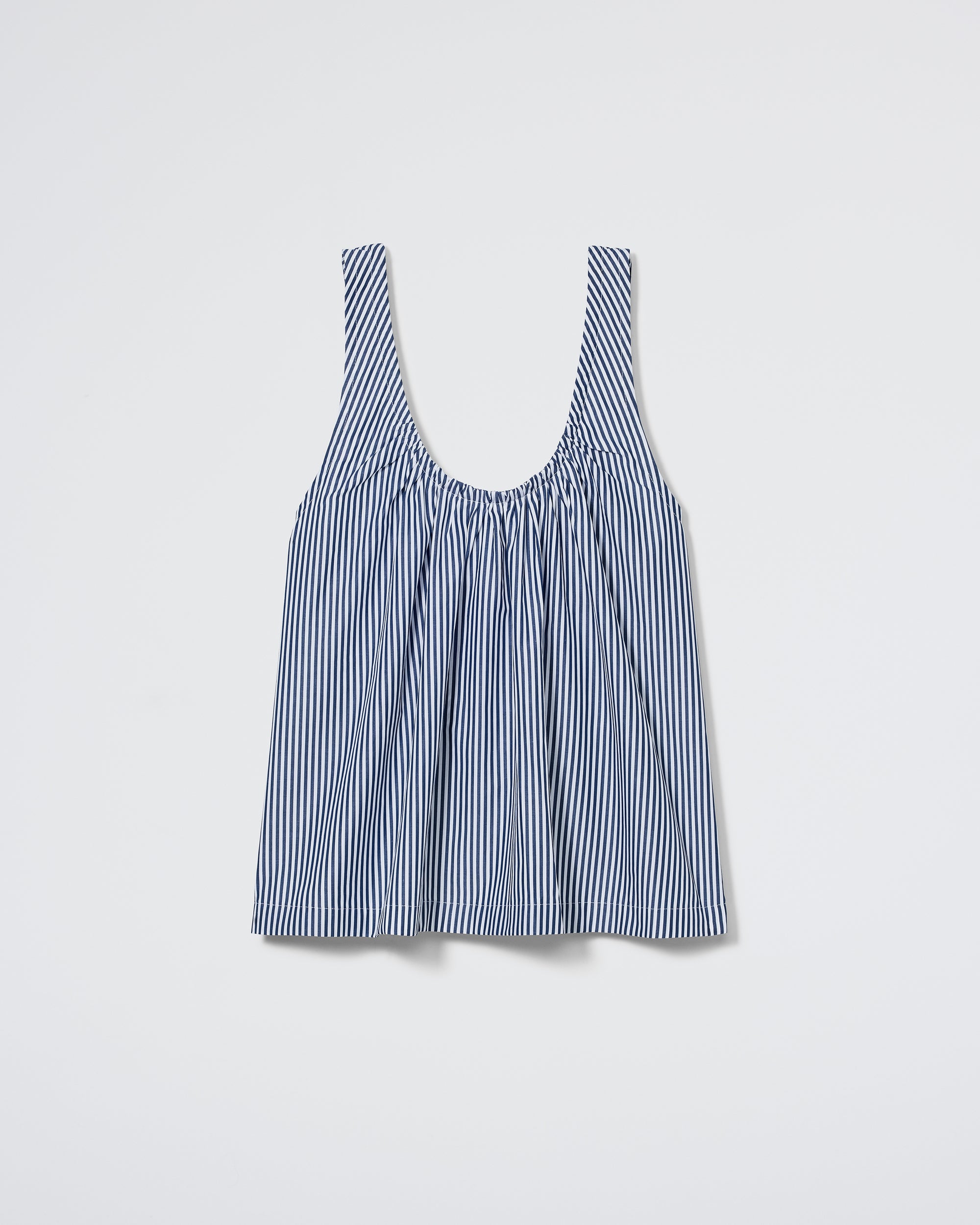 The Daydream Tank by Daphne features thin blue and white vertical stripes, a scoop neckline, and gathered chest detail. This sleeveless, loose-fit top in Midnight Stripe is shown against a plain light background.