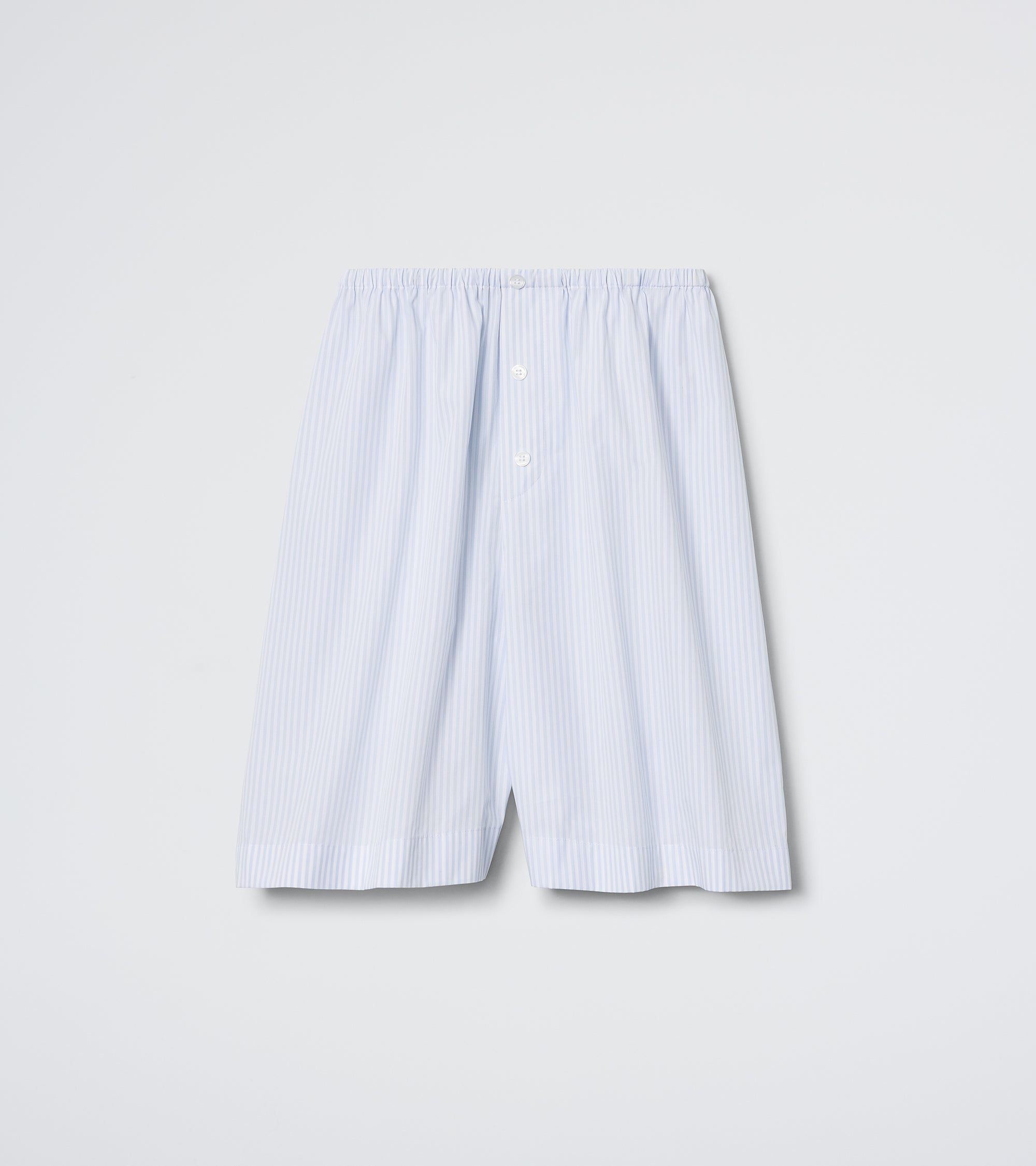 The Do Not Disturb Short - Cloud Stripe by Daphne features light blue and white vertical stripes, crisp poplin fabric, an elastic waistband, two white front buttons, and an embroidered back pocket, shown against a plain white background.